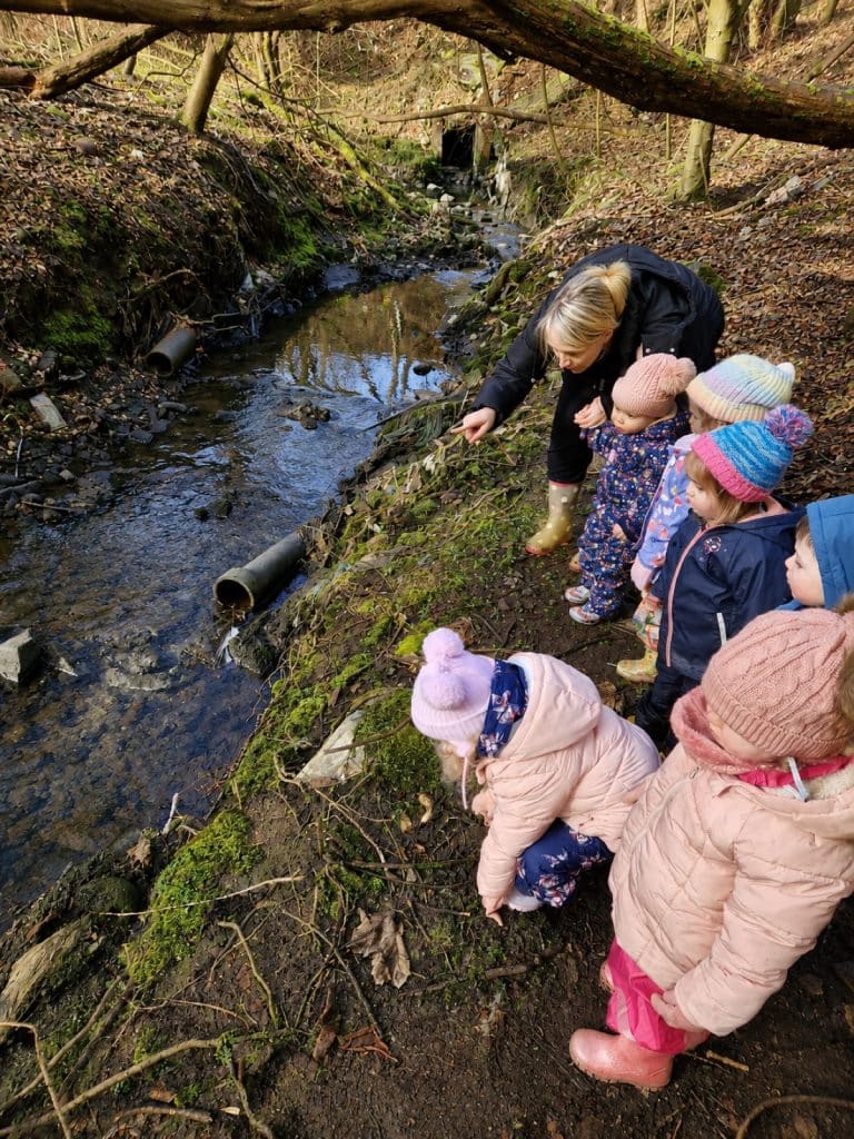 Nursery staff and children exploring a burn on a woodland walk